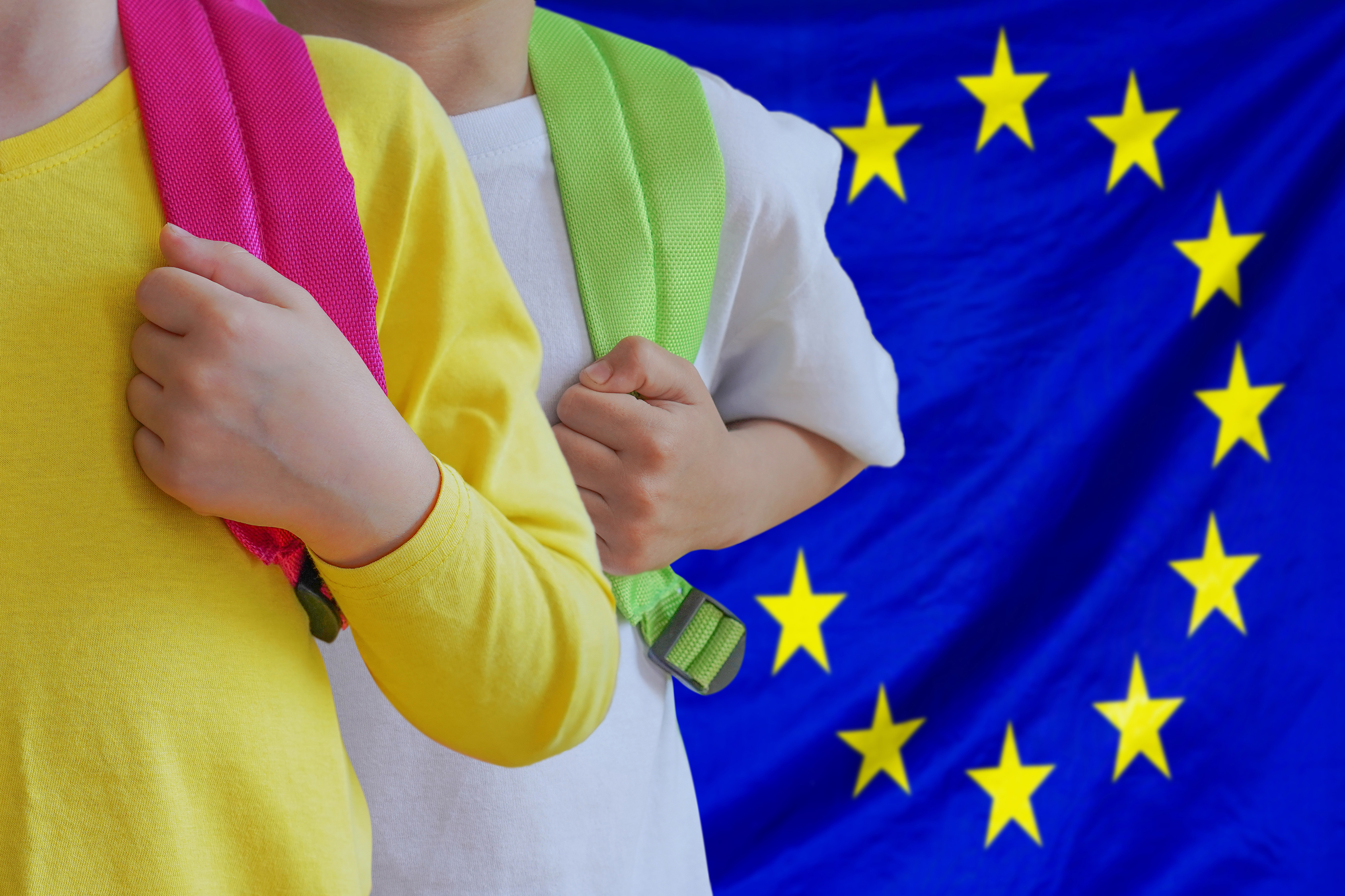 Two kids with satchels background of EU flag