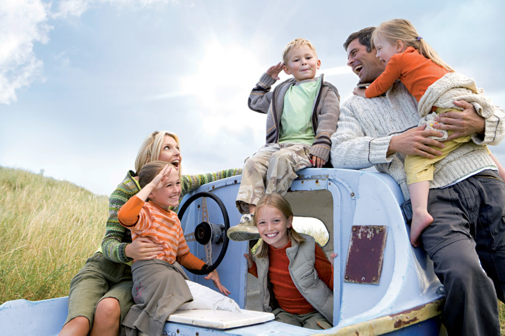 Young family sitting on boat at beach saluting
